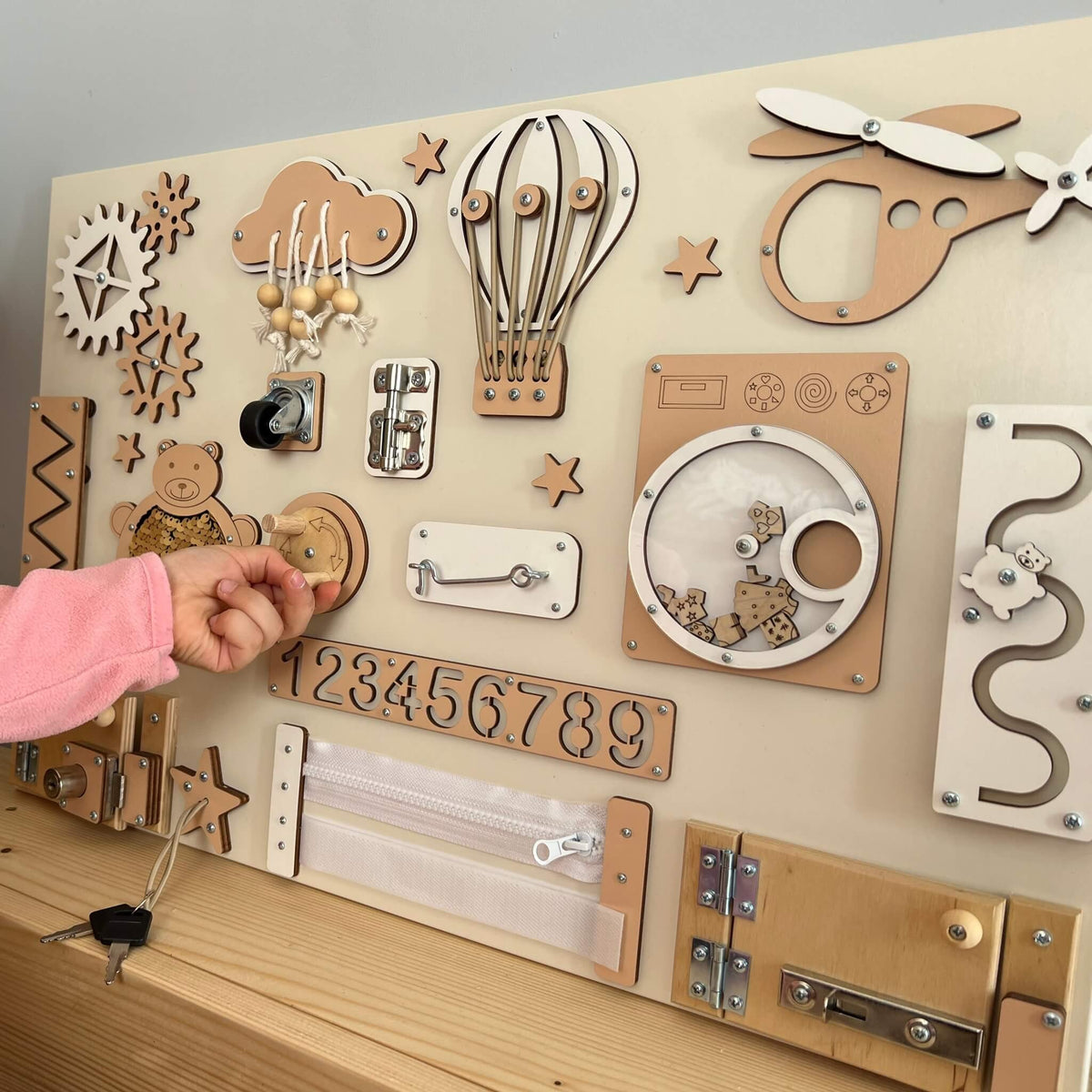 Dítě si hraje s activity boardem s dvířky a zámky BusyBunnyToys 40 × 60 cm, béžové provedení
