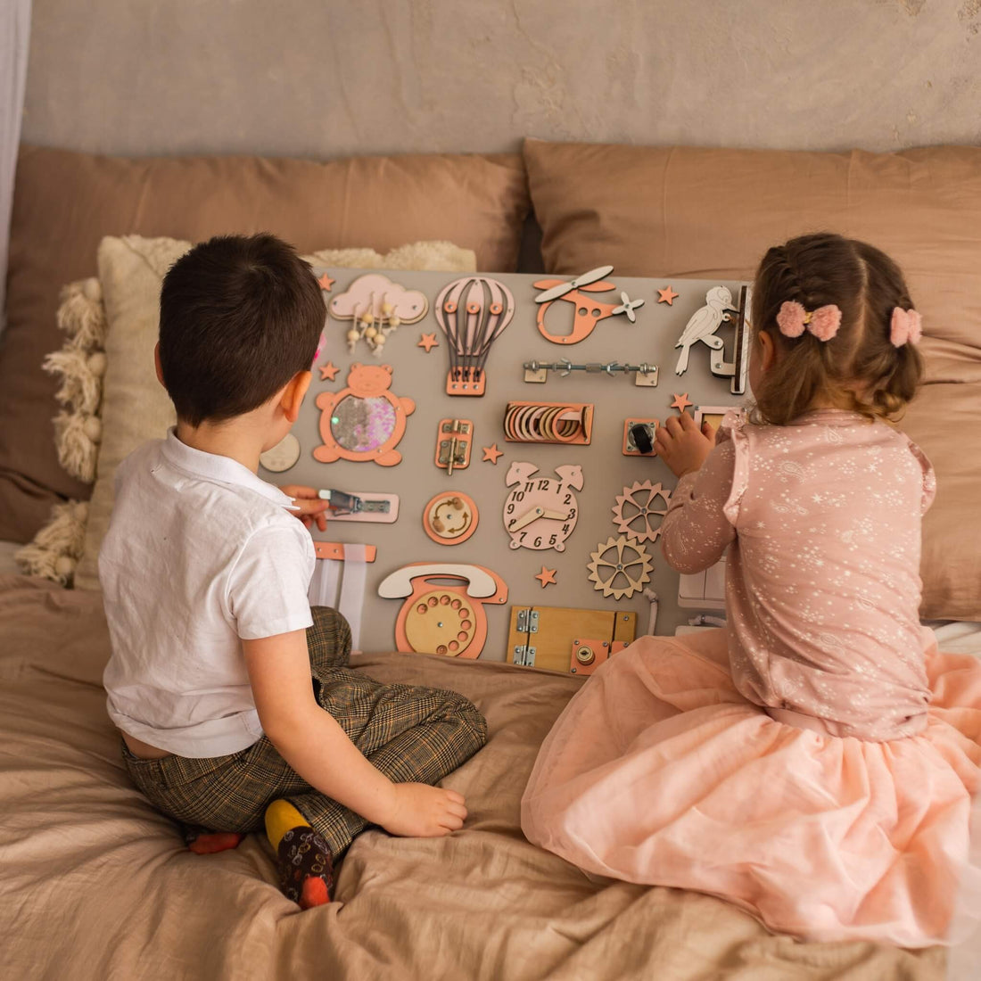 Dvě děti si na posteli hrají s activity boardem BusyBunnyToys 50 × 60 cm