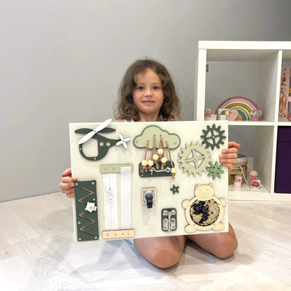 Holčička drží přenosný senzorický activity board BusyBunnyToys 30 × 40 cm, šalvějově zelené provedení